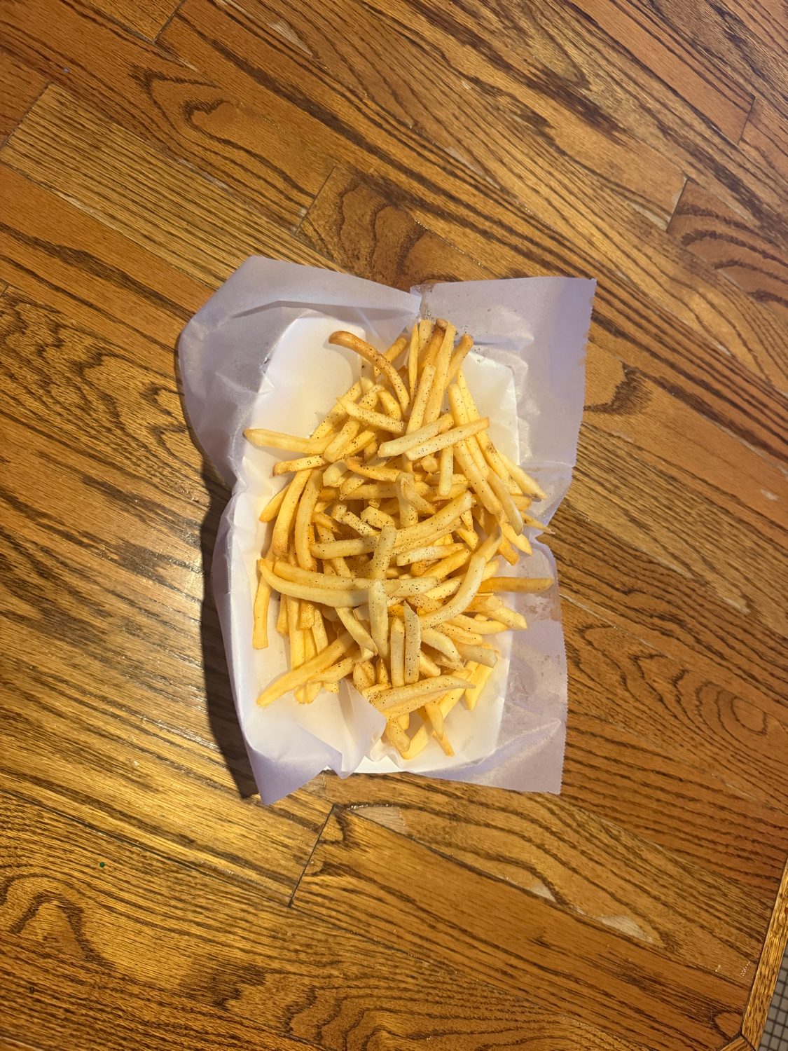 Basket of seasoned fries in paper on a wood table