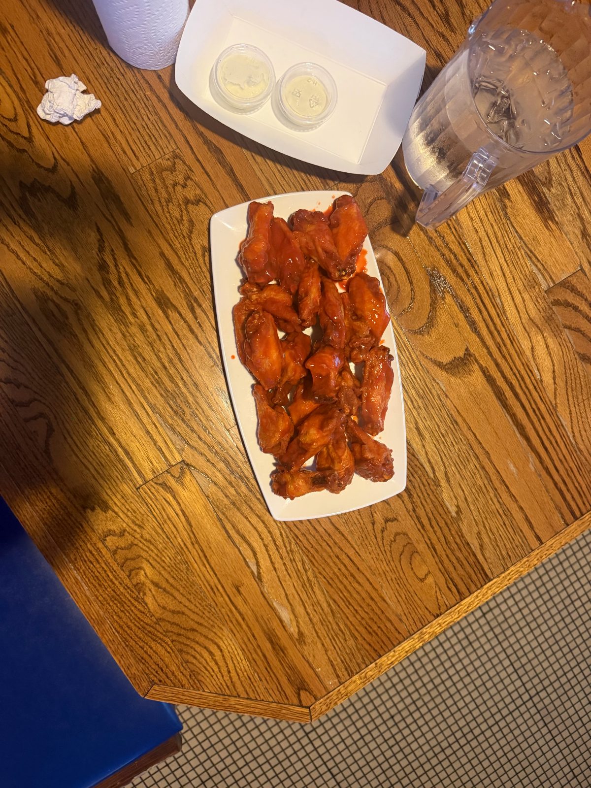 Platter of buffalo wings with two cups of blue cheese on a wood table