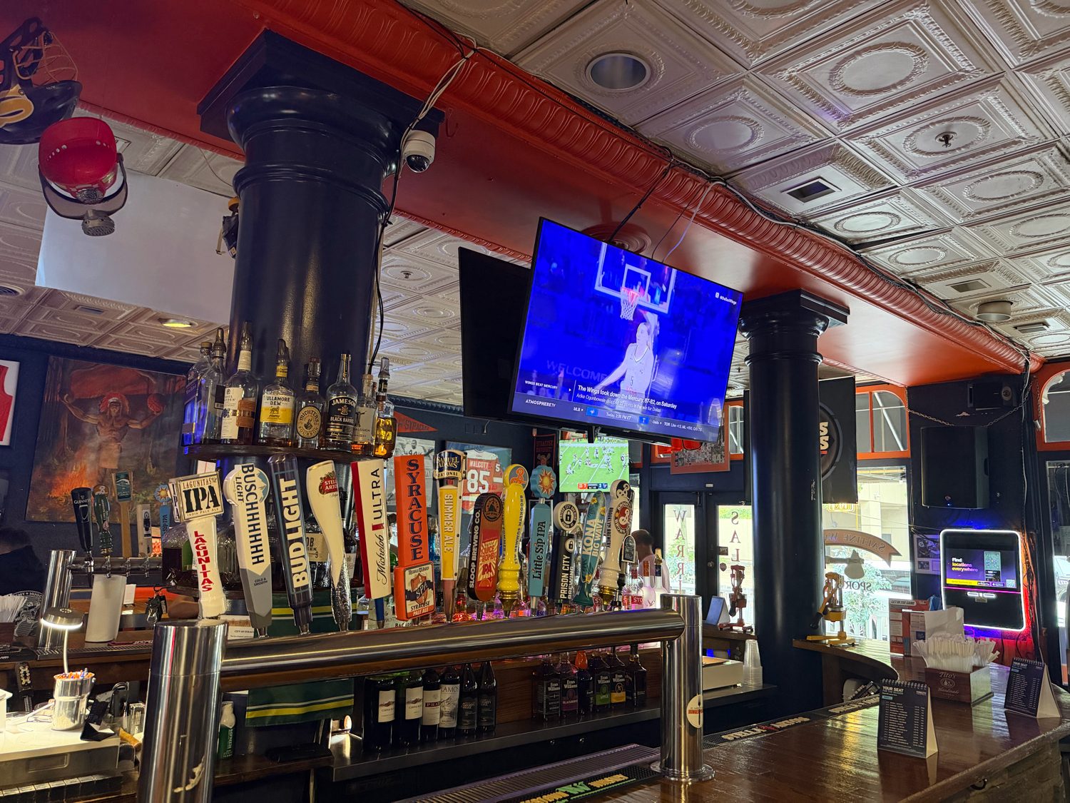 The main bar at Saltine Warrior: a long row of taps, pressed-tin ceiling and screens showing the game