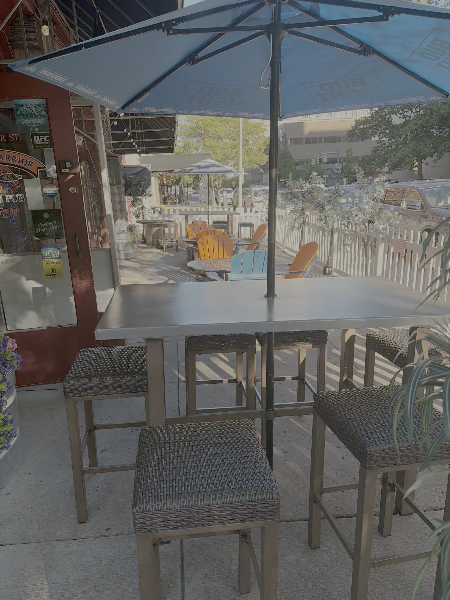 The front porch on Water Street: high-top tables under Bud Light umbrellas, Adirondack chairs around a fire pit, and a white picket fence